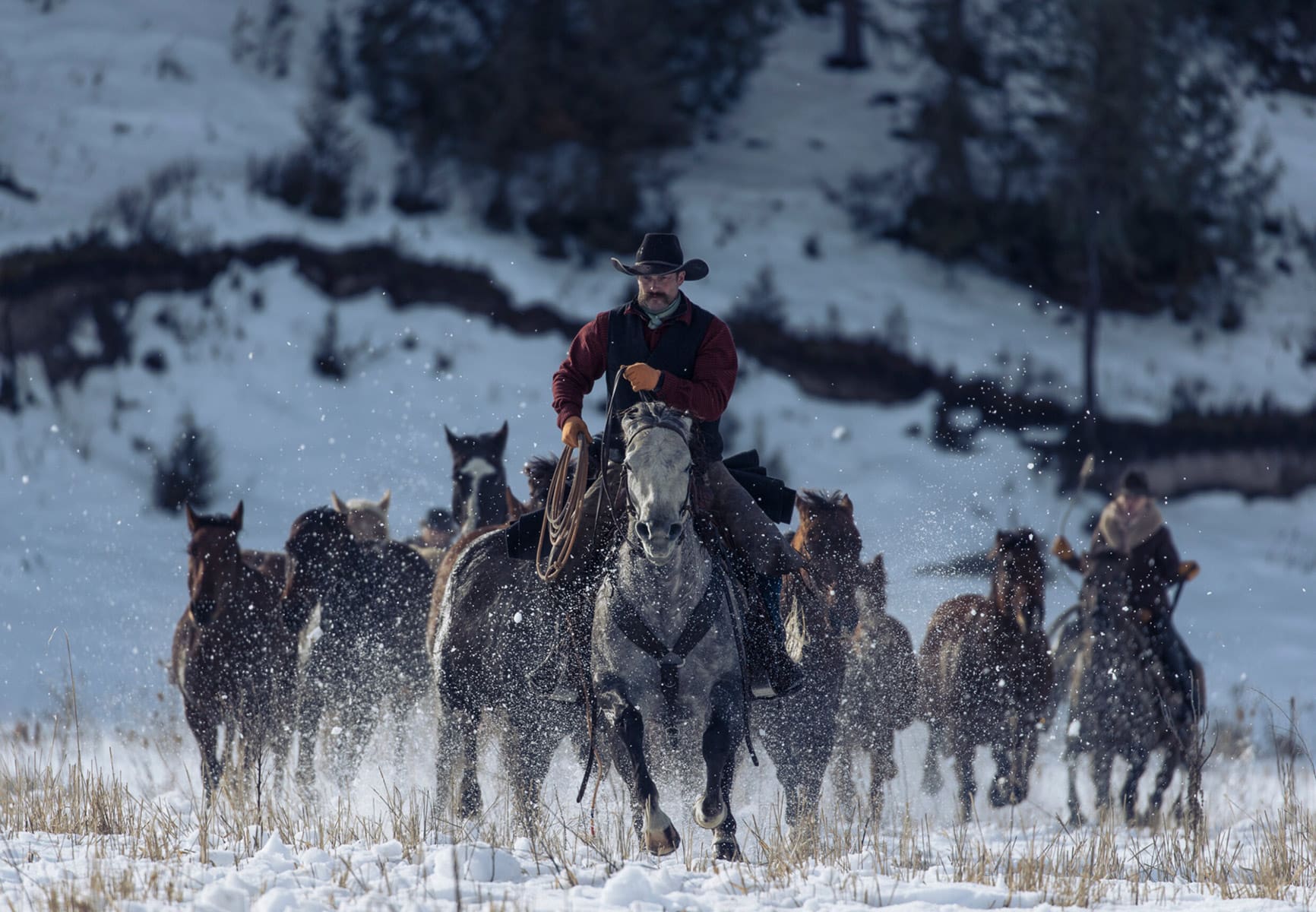 A rancher and cowboy brings in a heard of horses across a snowy landscape in Alaska.