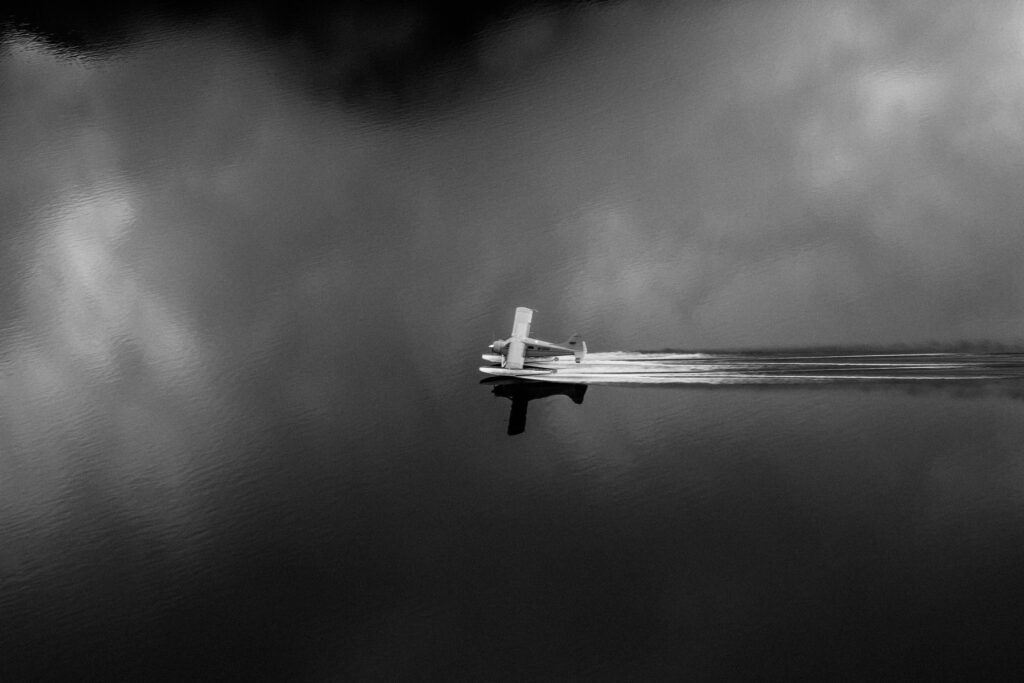 A seaplane lands on a lake in rural Alaska in this black and white image. 