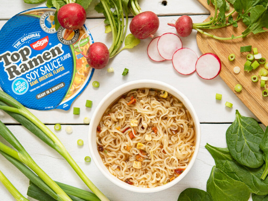 A bowl of Top Ramen on a table with vegetables.