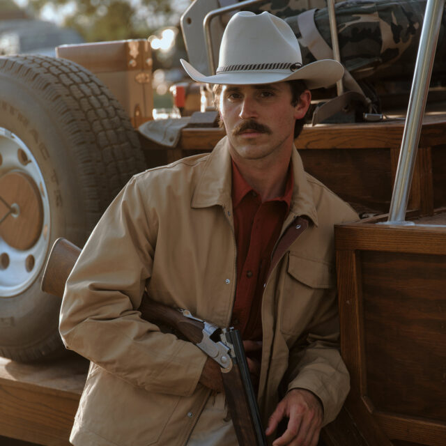 A rancher and hunter poses for portrait with his rifle and cowboy hat on his ranch in West Texas. Photographed by Travis Gillett.