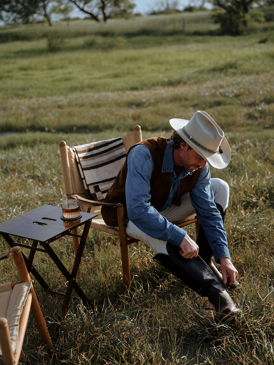 A hunter and rancher zips up his boots on his ranch in Texas. Photographed by Travis Gillett.