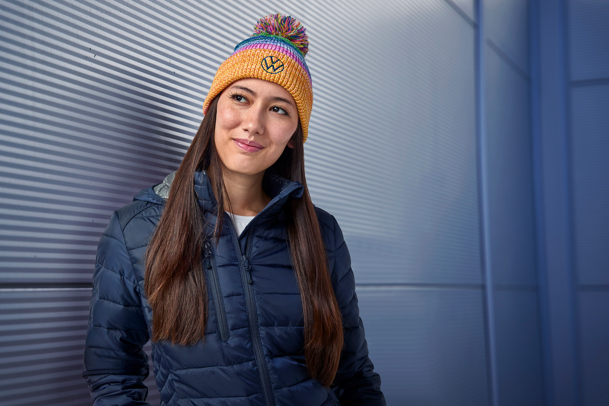 A young woman wears a multi-colored VW winter hat that she was photographed in for their winter catalog inside an e-commerce photo studio.