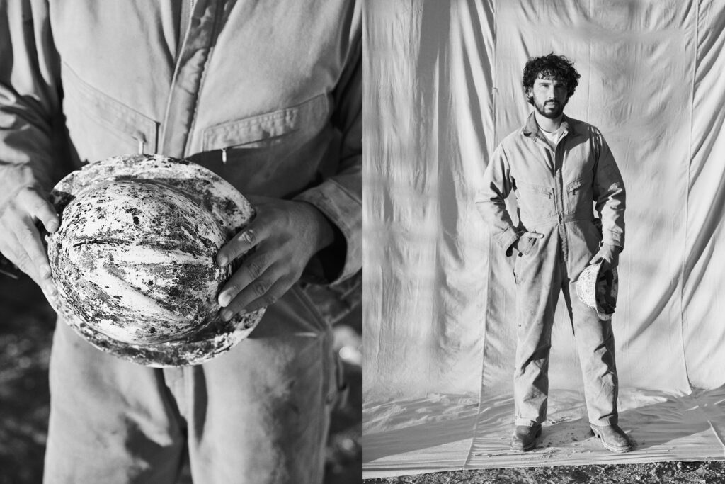 A construction worker holding his muddy helmet and standing for a portrait.