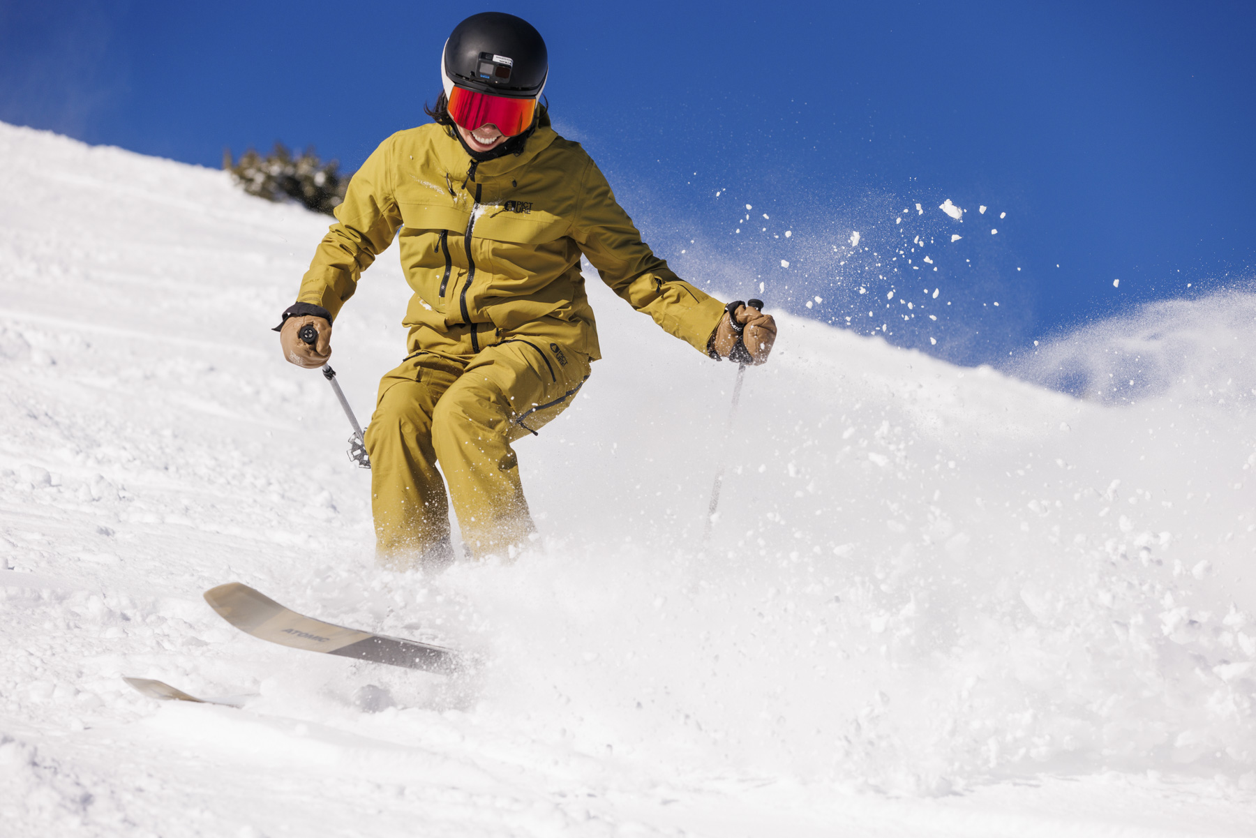 A skier in a yellow jacket, black helmet, and red goggles glides downhill through fresh powder snow under Idaho’s clear blue sky—a perfect winter sports scene captured by a commercial photographer.