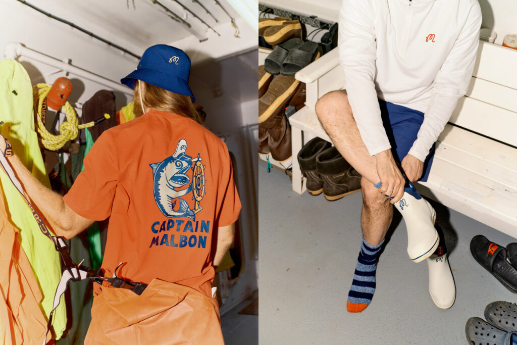 Two men in a mudroom: one in an orange Captain Malbon golf shirt and blue hat hangs gear; the other, in a white shirt, blue shorts, and striped socks, sits on a bench putting on white boots. Various shoes and clothes are around them.