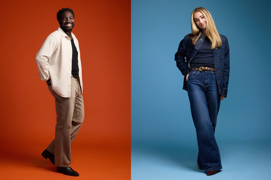A man in tan pants and a cream shirt stands smiling against an orange background, while a woman in blue jeans and a denim jacket stands with hands in pockets against a blue background.