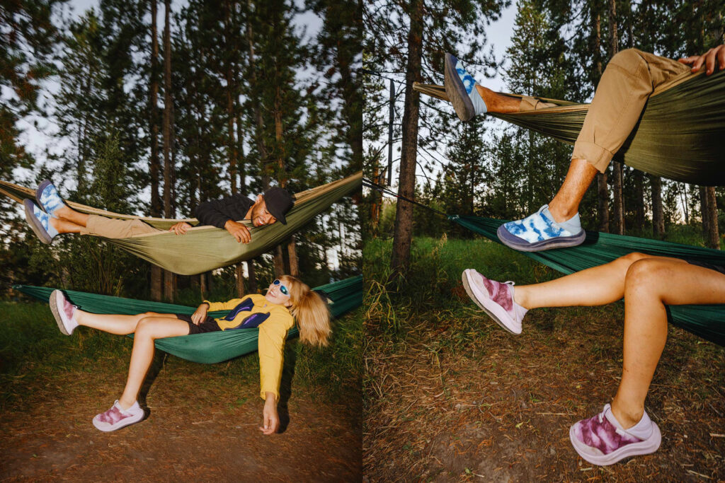 Two people relax in separate hammocks stacked one above the other in a forest. Both wear colorful slip-on shoes; the top person wears blue shoes and tan pants, and the bottom person wears purple shoes and sunglasses.