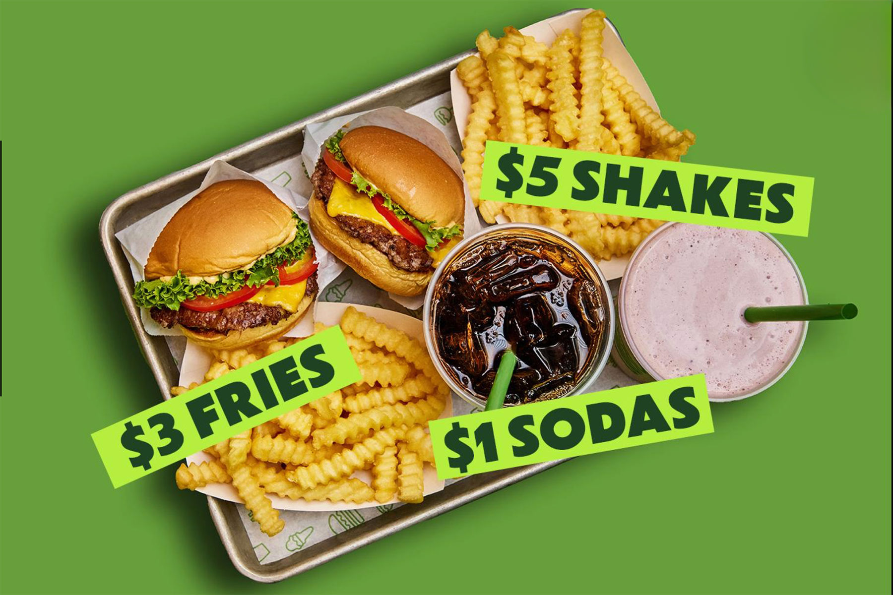 A tray with two cheeseburgers, two servings of crinkle-cut fries, a cola, and a milkshake on a green background. Text overlaid reads: $3 FRIES, $5 SHAKES, and $1 SODAS.